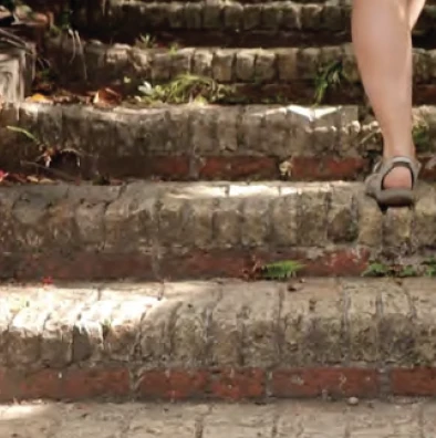 Close view of a person walking barefoot up worn brick steps, moss and fallen leaves between the courses.